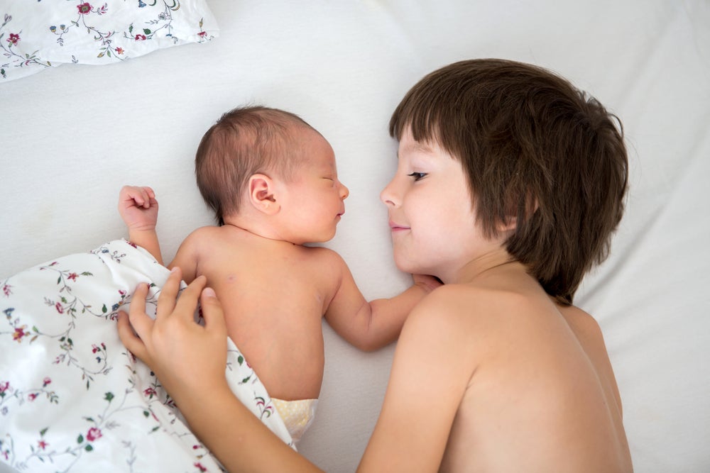 Beautiful boy, hugging with tenderness and care his newborn baby brother at home, Beautiful boy, hugging with tenderness and care his newborn baby